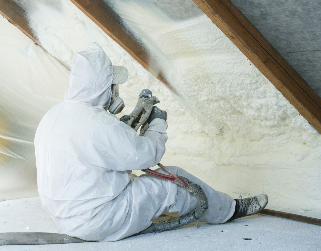Operatore professionale in abiti protettivi applica schiuma isolante sotto il tetto.