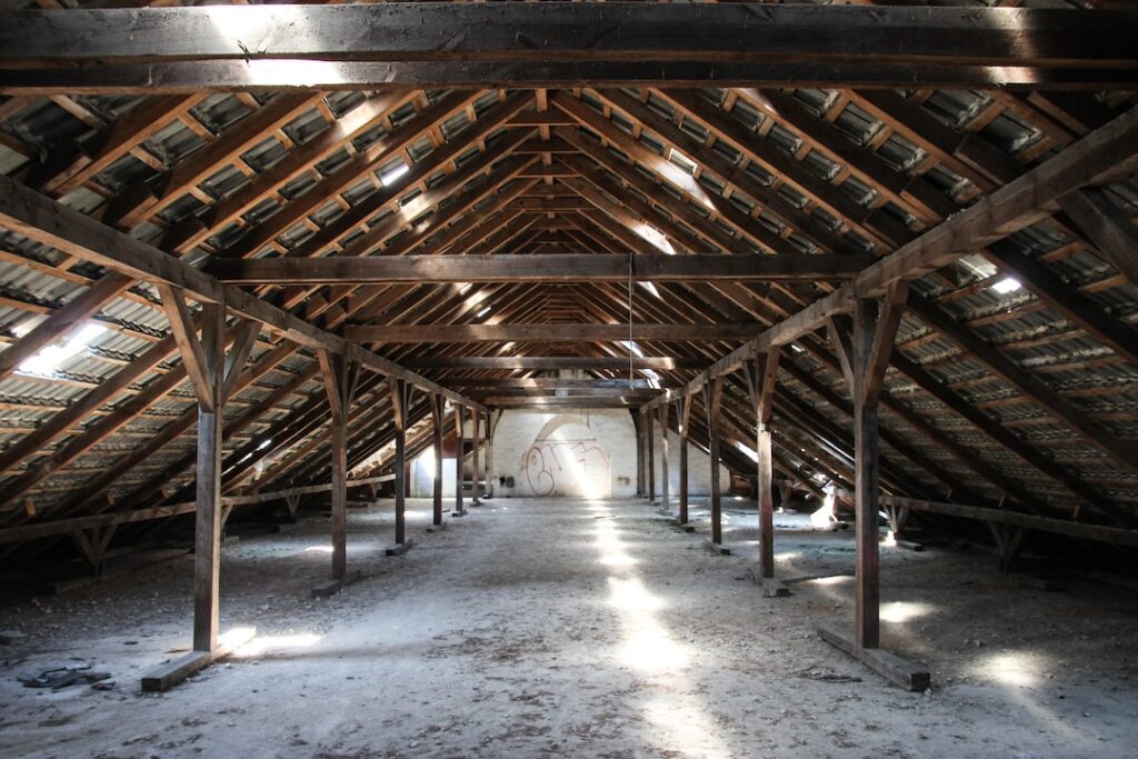 Interno di una mansarda abbandonata con travi in legno esposte e ampio spazio vuoto.